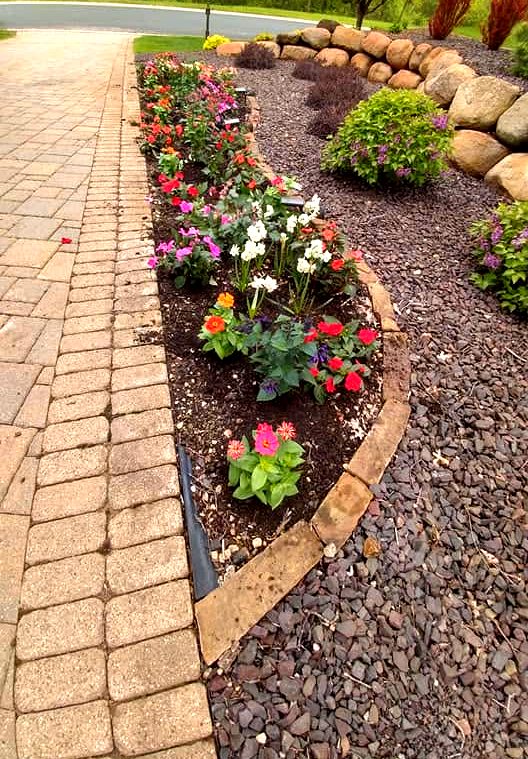 Curved annual flower bed with boulder retaining wall and paver edging